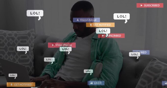 Animation of social media icons over african american man using laptop sitting on the couch at home