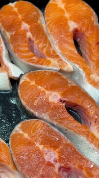 Fresh trout steaks on chilled shelf display, market presentation with ice crystals and glistening orange fillets, retail pricing.