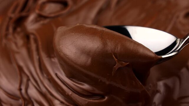 Spoon spreading and taking brown creamy melted milk chocolate spread close up