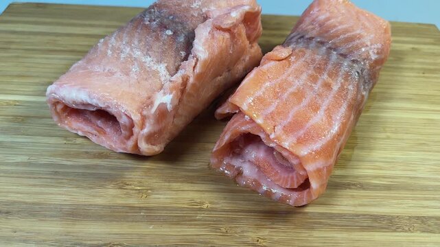 Raw frozen slices of salmon rolled up on cutting board