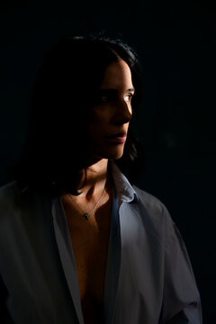 Woman in dim lighting with dramatic shadow on her face, wearing an open shirt. Milan, Italy