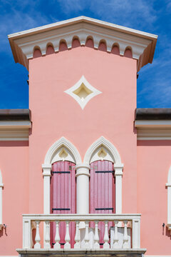 Pink building facade with arched windows and closed shutters against a blue sky. Caorle, Metropolitan City of Venice, Veneto, Italy