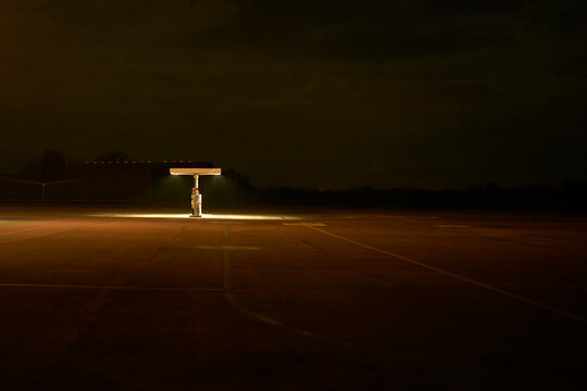 A lone person stands under a dimly lit gas station canopy at night in an empty parking lot. Zurich, Switzerland