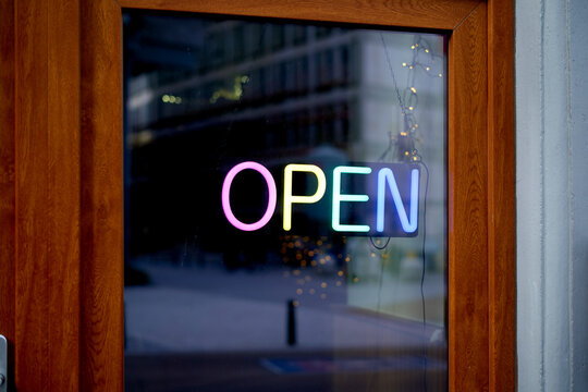 Neon open sign glows brightly in a window with a wooden frame. Brussels, Belgium