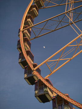 A section of a ferris wheel against a clear blue sky with the moon visible in daylight. Brussels, Belgium