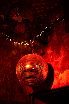 Red-lit mirrored disco ball with string lights and a wall fan in the background. Belgium