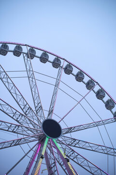Ferris wheel against a pale blue sky, illuminated with colorful lights at dusk. Belgium