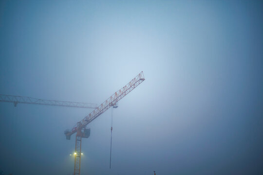 Construction crane emerging from fog against a blue-gray sky at dawn. Brussels, Belgium