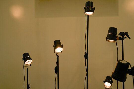 Six spotlights with glowing bulbs on stands against a plain wall. Brussels, Belgium