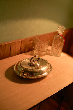 Silver dish with intricate handle next to crystal glass and decanter on wooden table. Brussels, Belgium