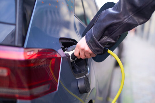 Hand plugging a yellow cable into an electric car's charging port on a city street. Brussels, Belgium
