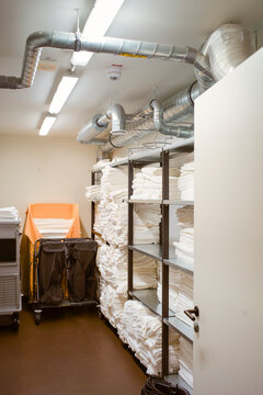 Storage room with shelves of neatly folded white linens and industrial ceiling pipes. Brussels, Belgium