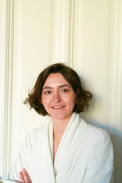 Woman with short hair smiling in a white robe against a light background Brussels, Belgium