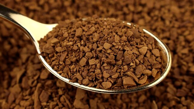 Brown instant freeze-dried coffee in a spoon with background circle rotation close up
