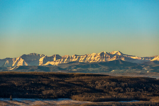 Majestic mountain range under clear blue sky with sunlit peaks and shadowed forest landscape. Close to Calgary, Canada