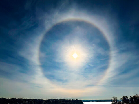 Bright sun halo in a clear blue sky over a landscape with trees and water. Canada