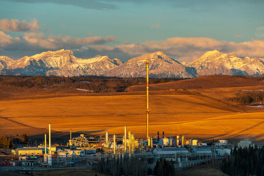 Industrial plant situated against a backdrop of vast mountains and expansive fields. Close to Calgary, Canada