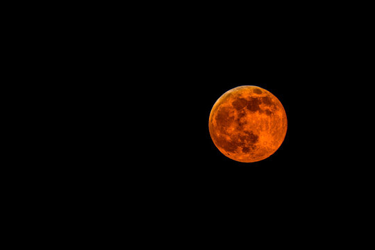Blood moon glowing red-orange against a dark night sky. Canada