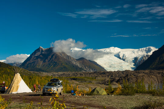 Camping site with tents and vehicle near mountains and a glacier under a clear blue sky. Wrangell?St. Elias National Park, Alaska, USA