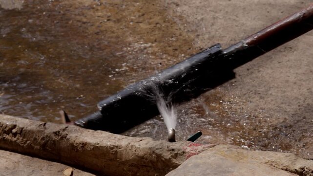 Close-up of water flowing from pipe with splashing droplets, representing irrigation system, water supply, infrastructure and environmental resource management concept.