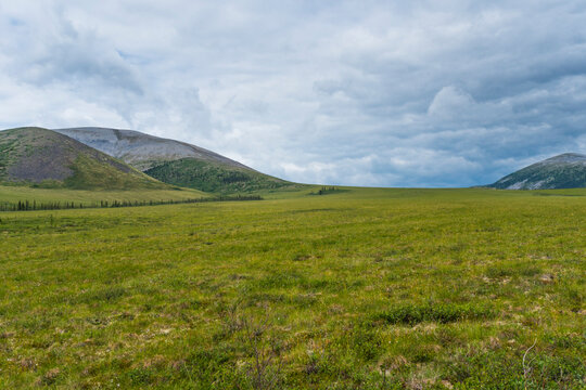 Vast green meadow with rolling hills under a cloudy blue sky. Canada