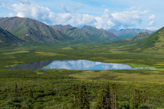 Majestic mountainous landscape with a serene lake and lush green valley under a blue sky. South Central Alaska, USA