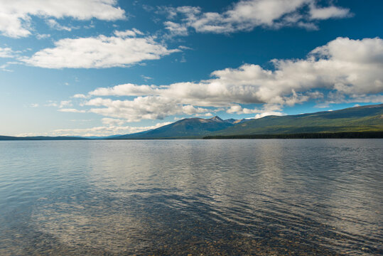 Tranquil mountain lake landscape with clear blue sky and fluffy white clouds. Yukon Territory, Canada