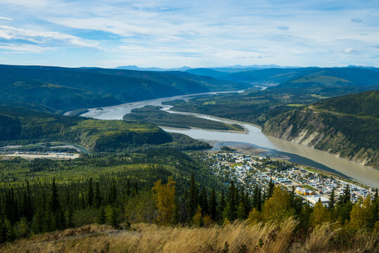 Scenic view of a river winding through lush green mountains and a small town below. Dawson City, Canada