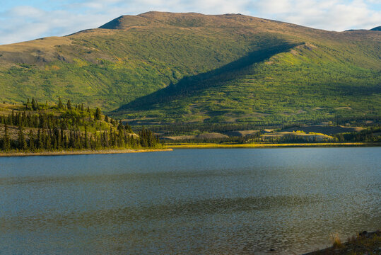 Serene lake with lush green hills in the background under a blue sky. Yukon Territory, Canada