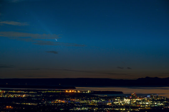 Night skyline with a comet streaking across the dark blue sky above a cityscape. Anchorage, Alaska, USA