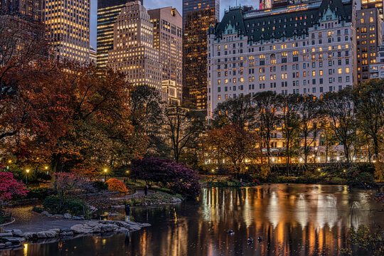 City skyline at dusk with reflections on a tranquil park pond and autumn foliage. Central Park Lake, New York City, USA