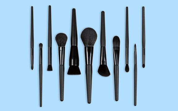 Black makeup brushes arranged on a light blue background in a symmetrical pattern.