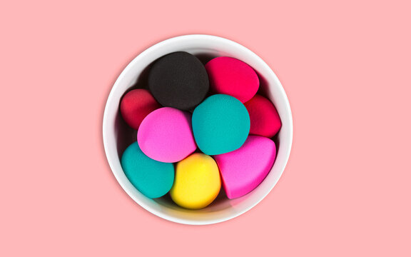 Bright colorful makeup sponges in a white bowl on a pink background.