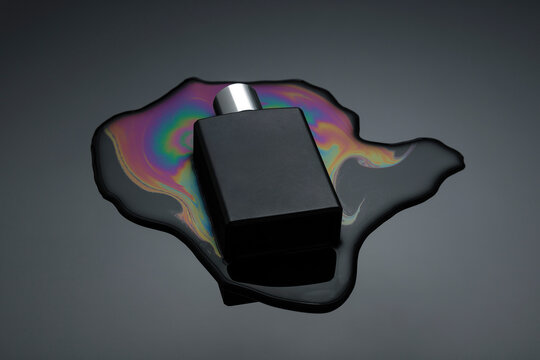 Black perfume bottle on a reflective surface with a colorful oil spill pattern beneath.