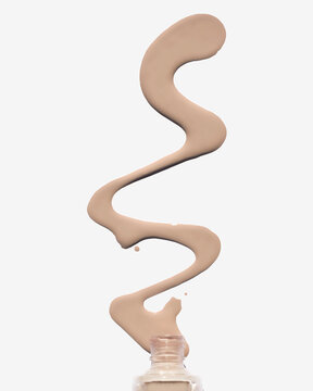 Liquid foundation swirling in the air from an open bottle against a white background.