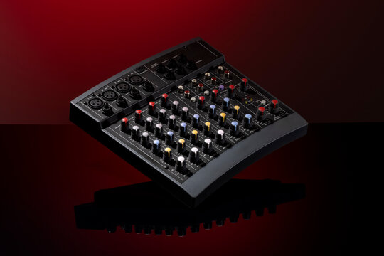 Black audio mixer with colorful knobs on a reflective surface against a red background.