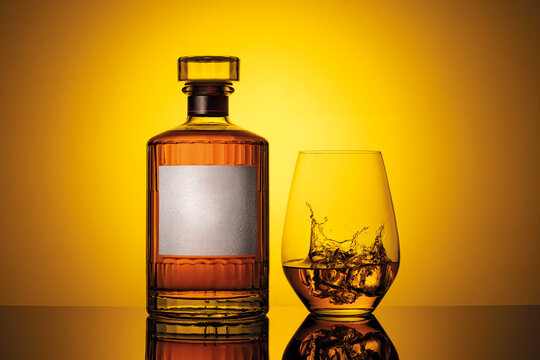 Whiskey bottle and glass with ice against a vibrant yellow background.