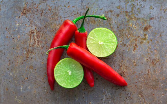 Red chili peppers and halved limes on a textured metal surface.