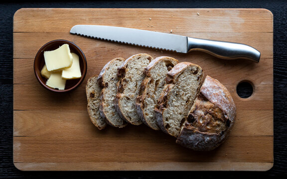 Sliced round bread with knife and butter on a wooden board.