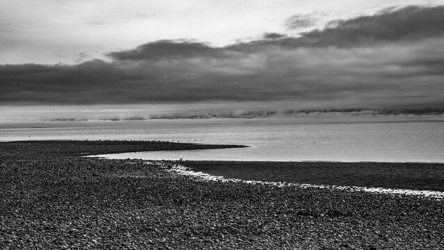 Stormy sky over a desolate pebble beach with calm sea in black and white. Qualicum Bay, Vancouver Island, British Columbia, Canada