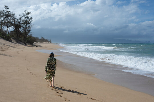 Person walks barefoot along a deserted beach with cloudy skies in the background. Paia, Maui, Hawaii, USA