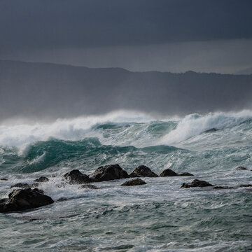 Stormy ocean waves crash against rocks under a dark, cloudy sky. Hookipa Beach, Maui, Hawaii, USA