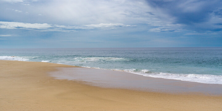 Tranquil beach scene with golden sand meeting the calm blue ocean under a cloudy sky. Punta Labos Beach, Todos Santo, Mexico