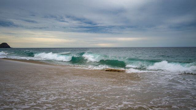 Ocean waves crashing on a sandy beach under a cloudy sky. Punta Labos Beach, Todos Santo, Mexico