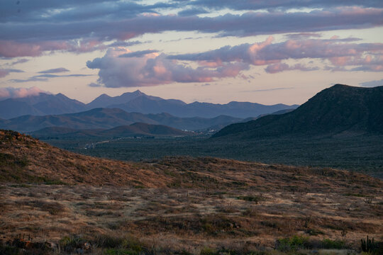 Scenic desert landscape with mountains, valleys, and a vibrant pink-hued sky at sunset. Todos Santos, Baja California, Mexico