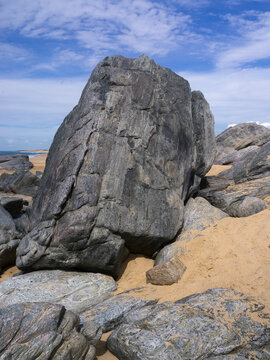 Large gray rocks on a sandy beach under a partially cloudy blue sky. Todos Santos, Baja California, Mexico