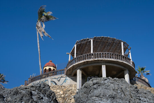 Round structure with open roof and palm tree against a clear blue sky on rocky terrain. Todos Santos, Baja California Sur, Mexico