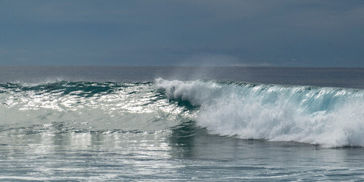Ocean waves breaking under a cloudy sky with a glistening water surface. Todos Santos, Baja California, Mexico