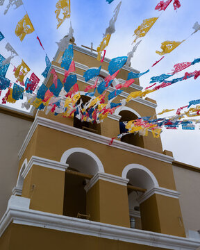 Colorful paper flags decorate a church tower under a bright blue sky. Todos Santos, Mexico