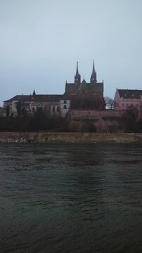 Vertical static shot of the Basel Minster (Basler M&uuml;nster) cathedral overlooking the Rhine river on a cold and misty morning.